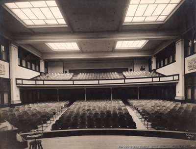 View from the auditorium stage toward wooden seats, the balcony and ceiling skylights