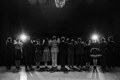 Black-and-white view of the Clue ensemble facing the audience under stage lights