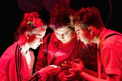 Three Tiger Drama performers gathered around a light under red stage lighting in The SpongeBob Musical, 2021