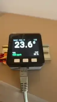The finished controller on the wall, its screen showing the room temperature in large digits with CO2 in ppm and humidity underneath, an Ethernet cable feeding it power from below