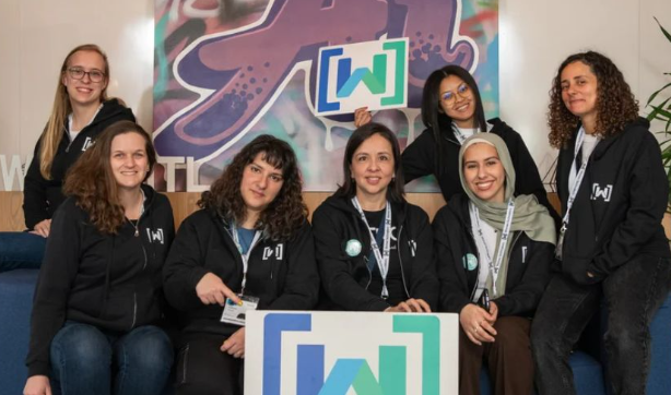 Group photo of seven Women Techmakers Ambassadors sitting on a couch behind a Women Techmakers logo sign