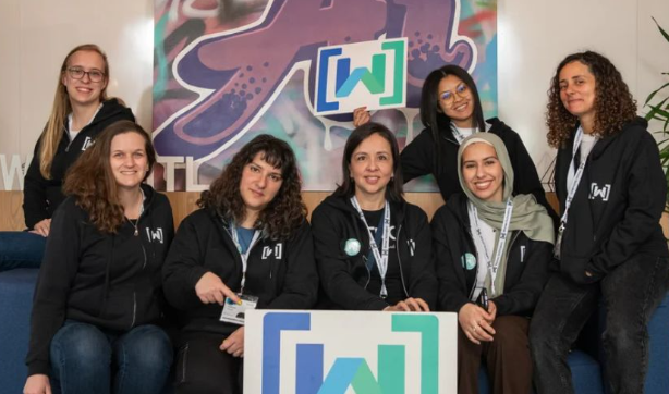 Women Techmakers logo tabelasının arkasındaki koltukta oturan yedi Women Techmakers Elçisi&#39;nin grup fotoğrafı