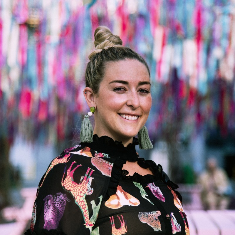 A photo of Hels, a white woman with a printed pattern blouse smiling at the camera