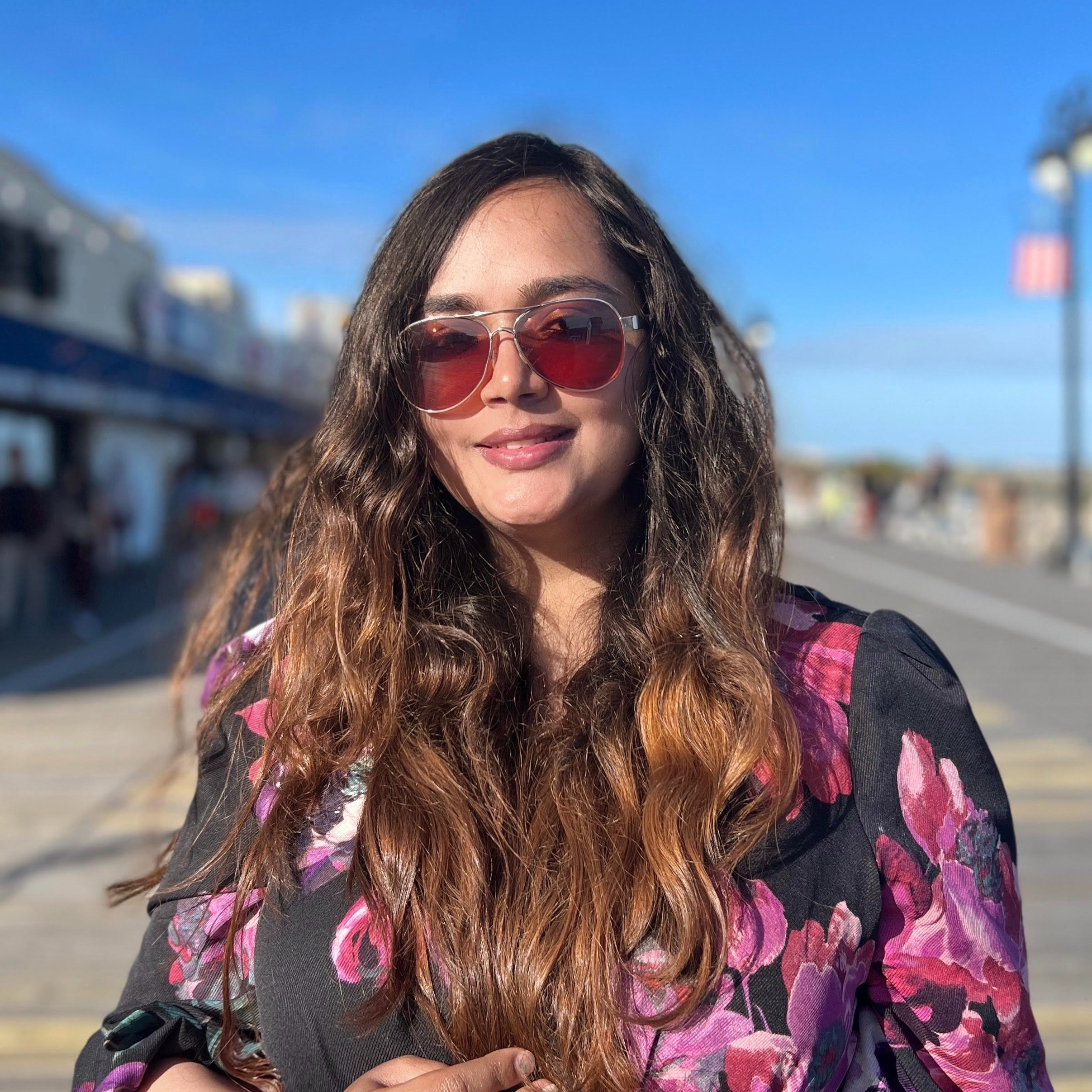 Retrato de Akshama sonriendo y con gafas de sol rojas al aire libre en un día soleado.