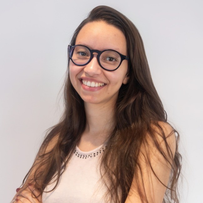 Bea, Brazilian woman with long brown hair and glasses, smiling at the camera.