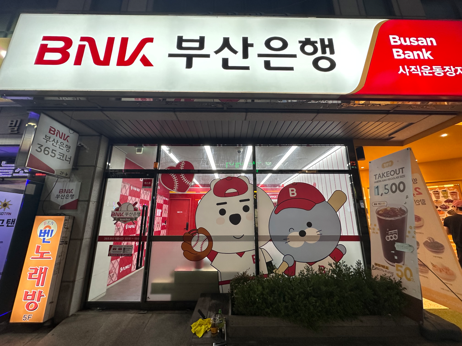 밤에 본 BNK 부산은행 사직운동장지점 외관과 유리에 붙은 캐릭터 그래픽