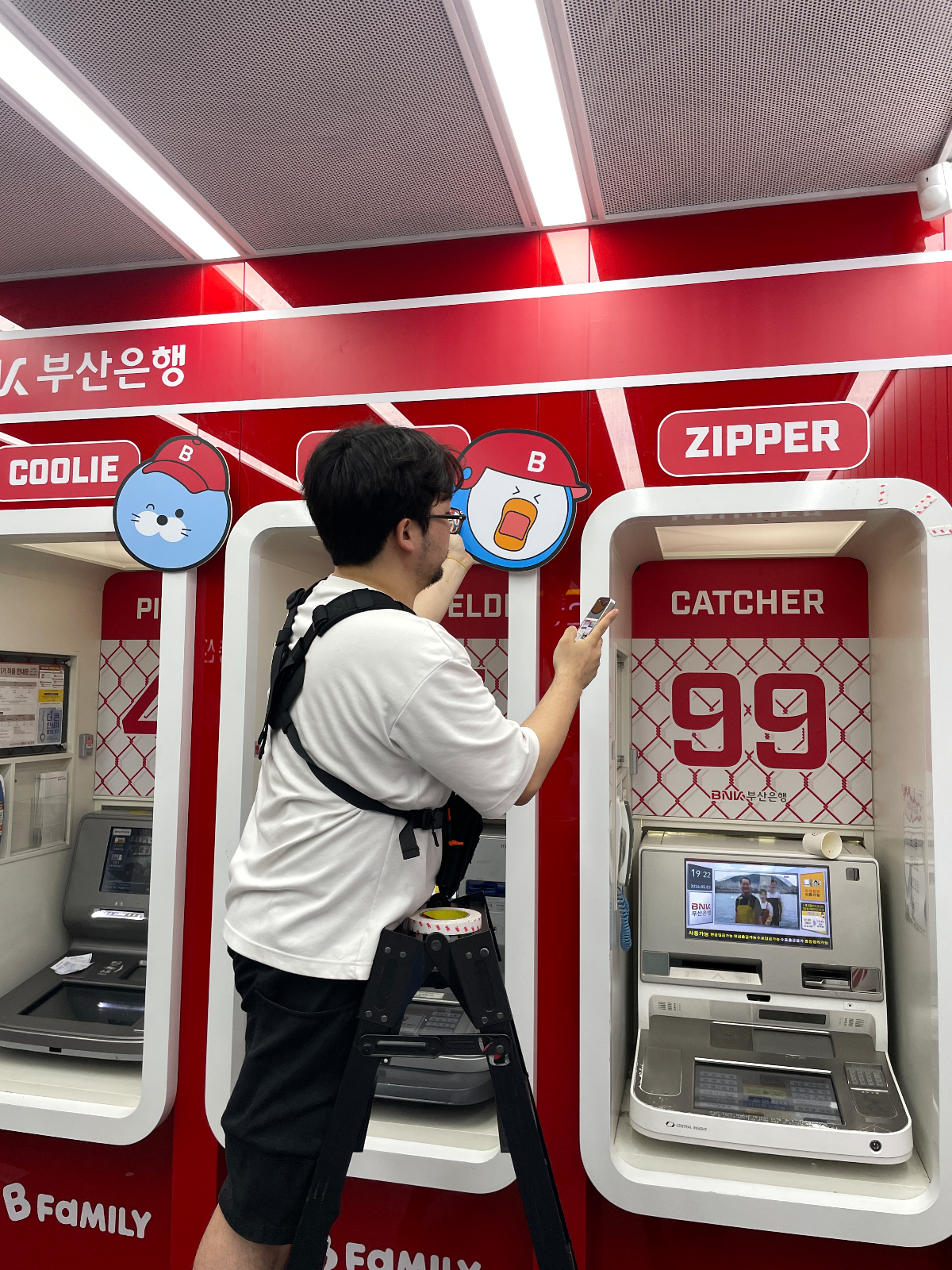 ATM 부스 상단 캐릭터 조형물을 손으로 눌러 고정하는 작업자