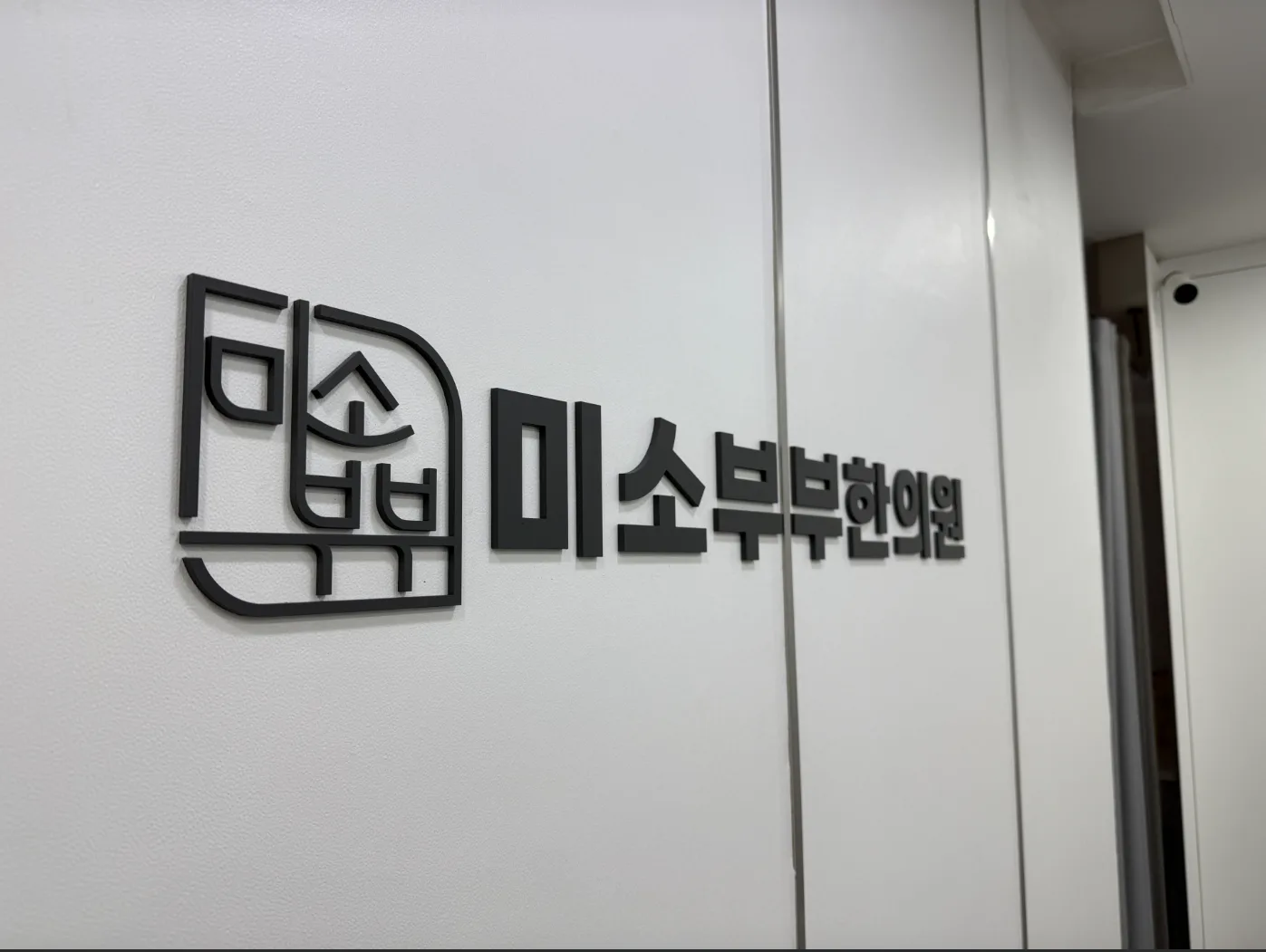 흰 벽에 붙은 검정 입체 로고와 한의원 상호