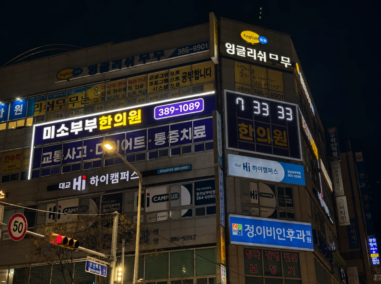 야간에 점등된 코너 건물 간판, 한의원 상호와 시계 숫자가 밝게 보인다