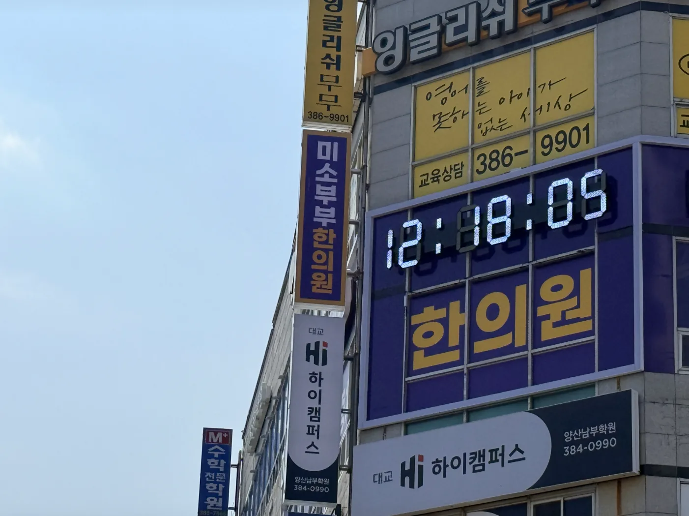 하늘을 배경으로 올려다본 세그먼트 시계와 세로형 한의원 돌출 간판