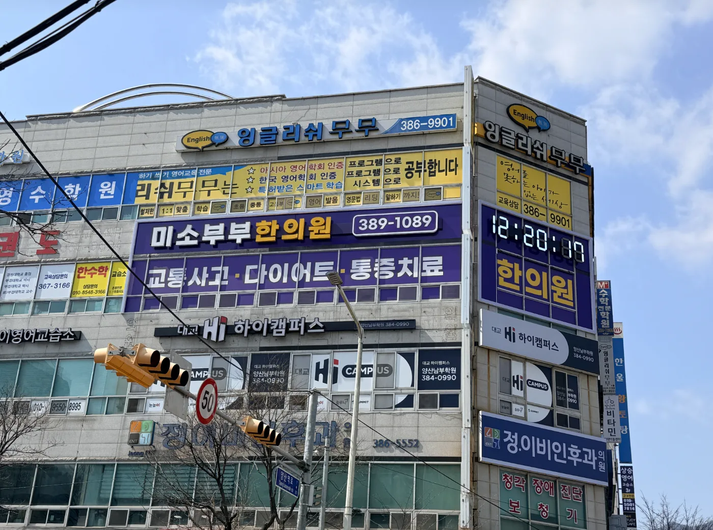 낮에 촬영한 사거리 코너 건물 전경, 여러 학원 간판 사이에 한의원 간판이 걸려 있다