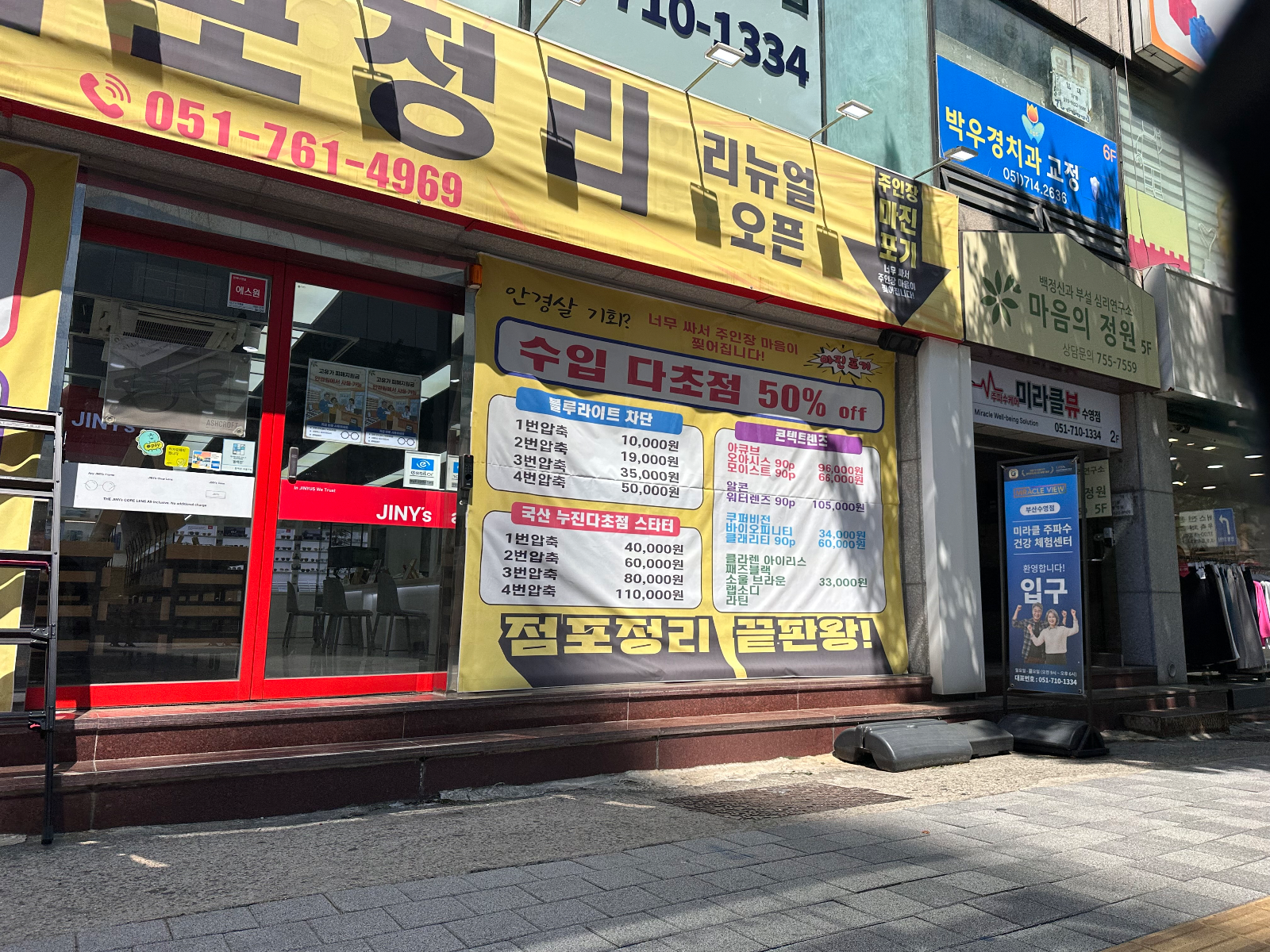 점포정리 문구와 렌즈 가격표가 인쇄된 현수막이 유리창과 간판을 가리고 있는 모습