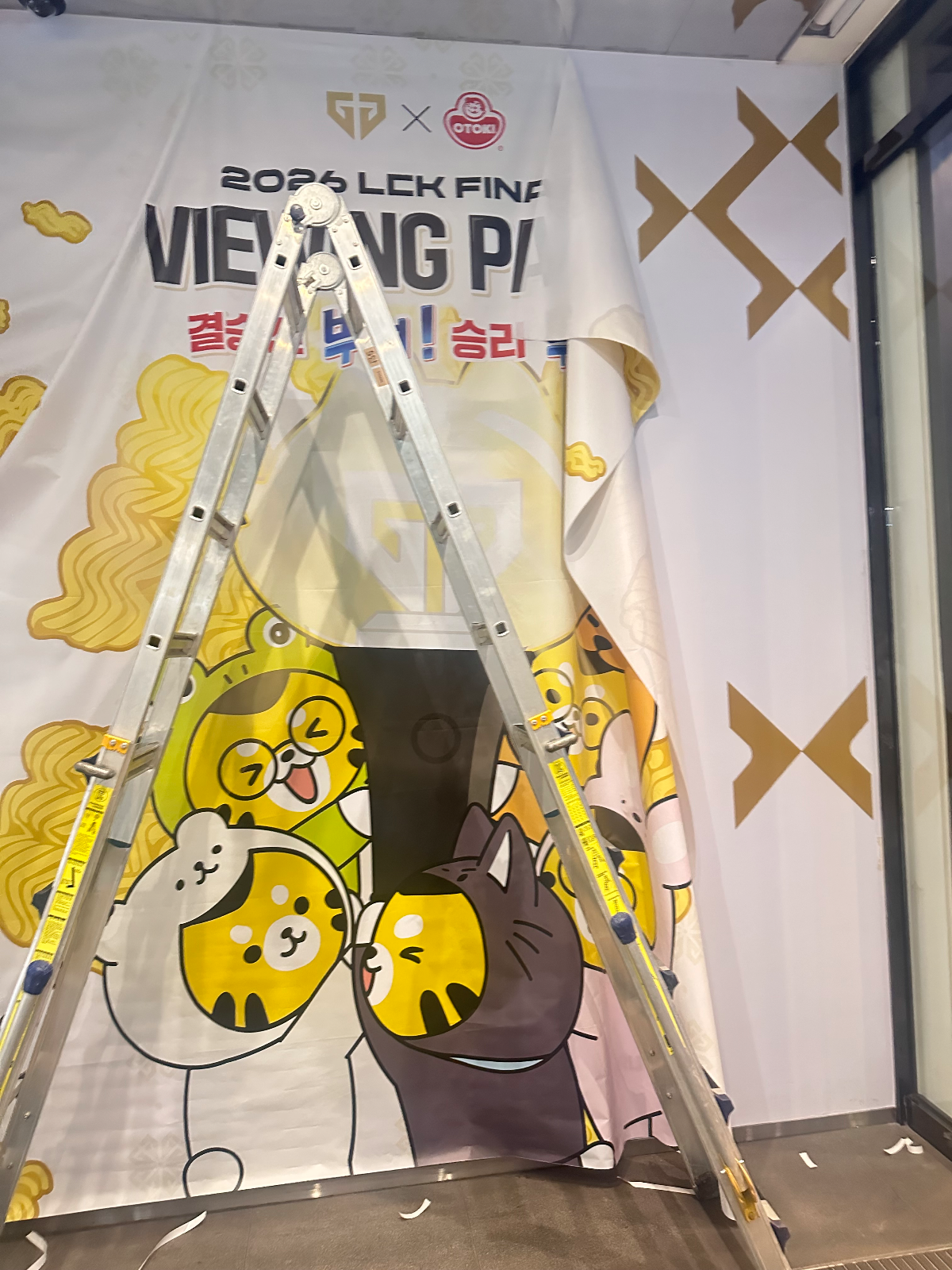 사다리를 걸치고 현수막 한쪽 모서리를 접어 올린 채 위치를 잡는 중