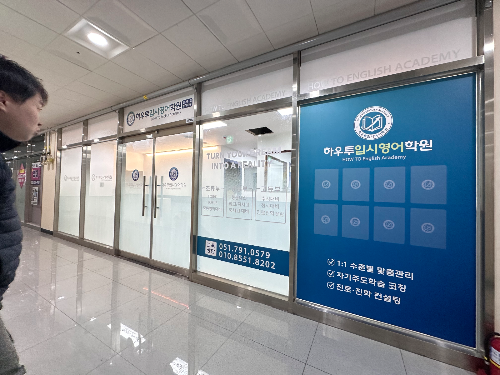 복도를 지나가던 사람이 학원 유리창을 바라보는 모습