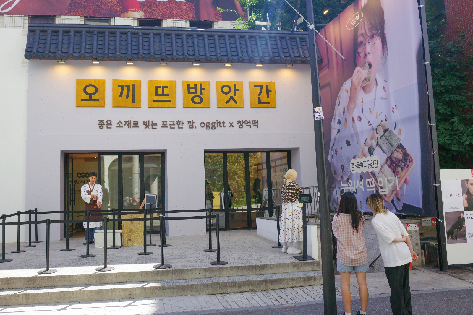 기와 지붕과 '오끼뜨방앗간' 나무 현판 간판이 달린 팝업스토어 외관, 오른쪽에 대형 현수막