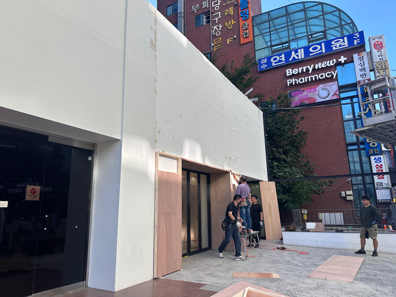 외벽 앞에서 합판을 들고 세우는 작업자 세 명