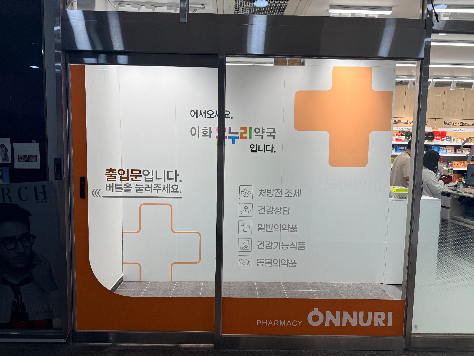약국 자동문에 시공된 시트지. 인사 문구와 취급 품목 아이콘, 하단 주황 띠
