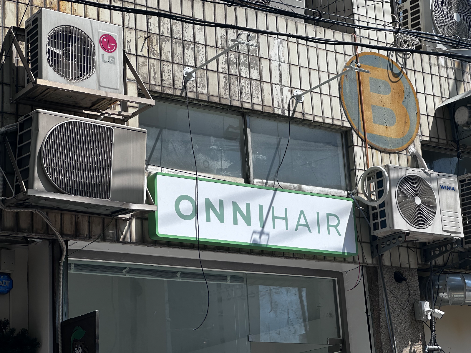 벽에 설치된 흰 바탕 초록 테두리 ONNIHAIR 간판과 그 위로 뻗은 흰색 지지대