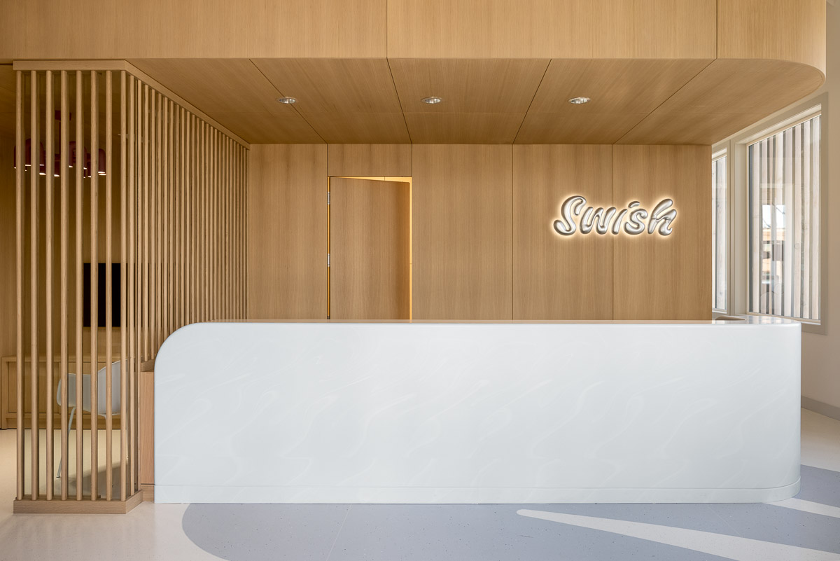 The front desk at Swish oral care featuring a white neon Swish logo sign, wood panelled walls and a white desk.