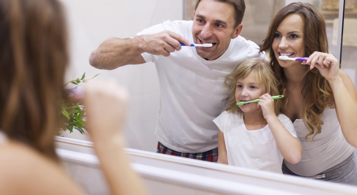 A family brushing their teeth together in the mirror.