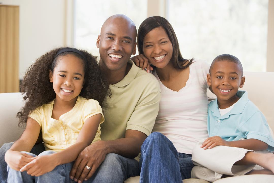 A family sitting on the couch and smiling.