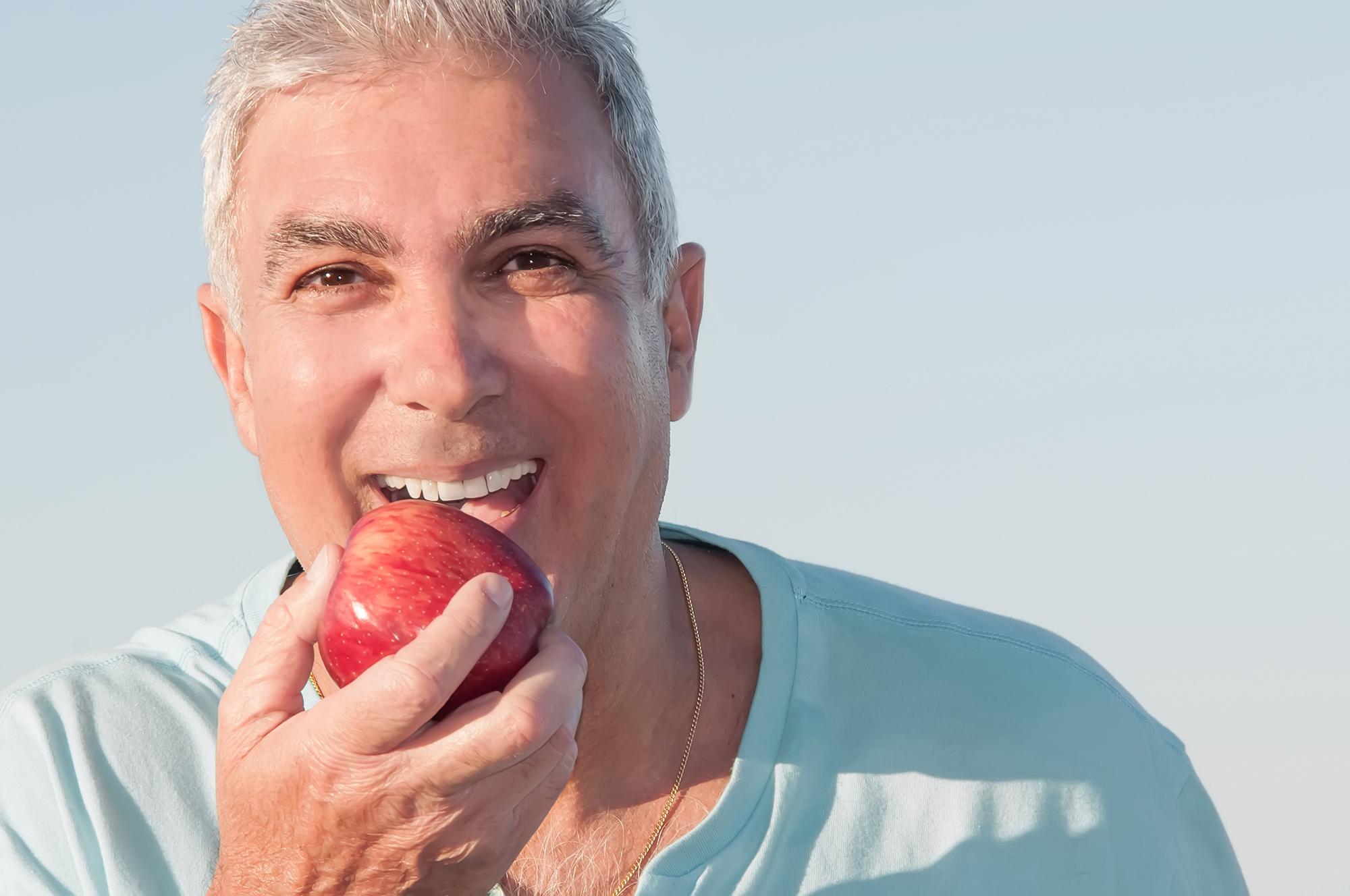 An older man biting into an apple.