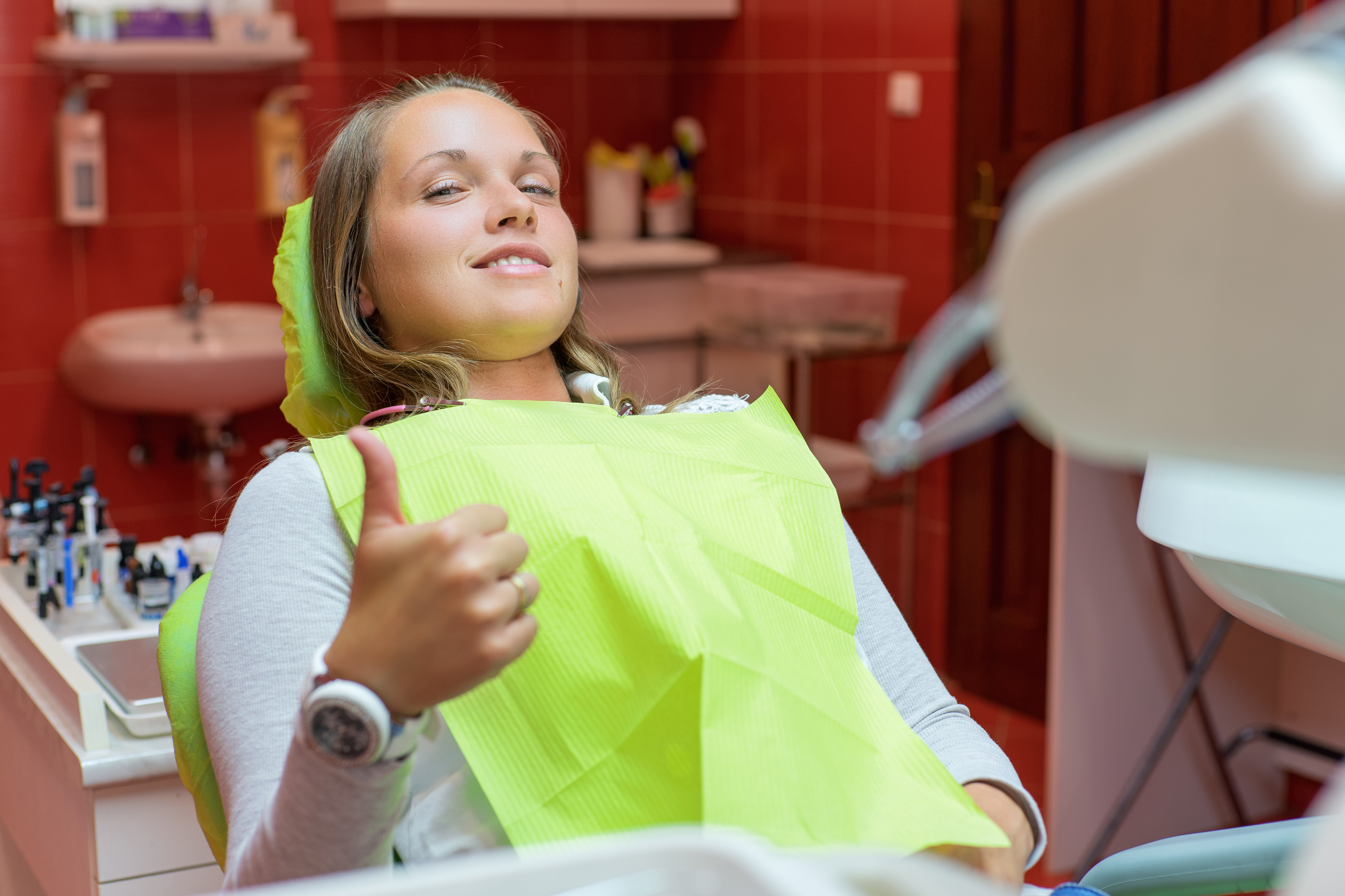 A woman looking sleept and giving the thumbs up at the dentist.