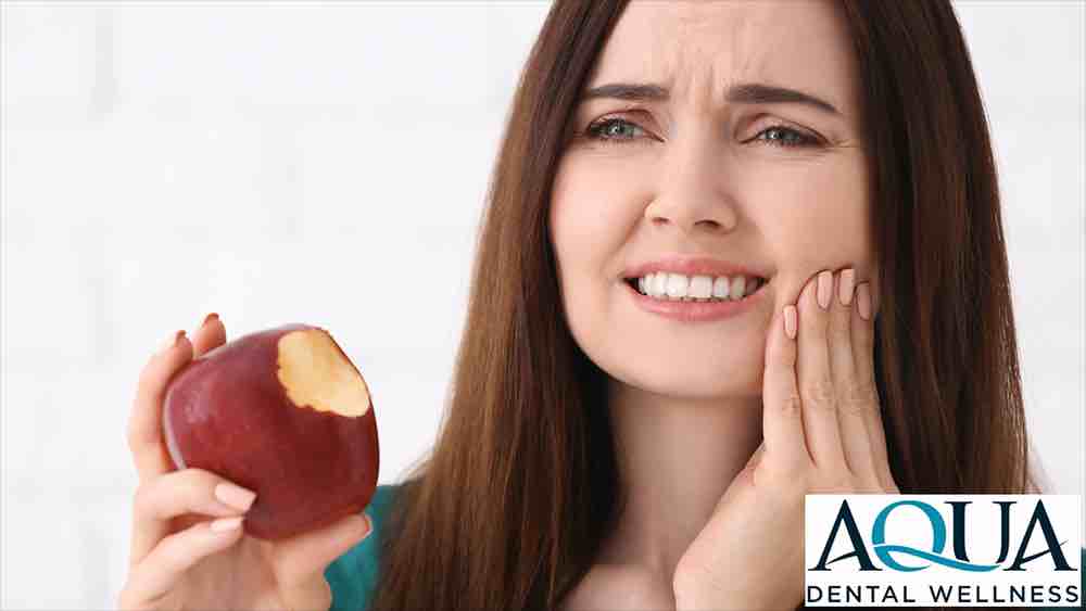 A person holding their jaw in pain while eating an apple.