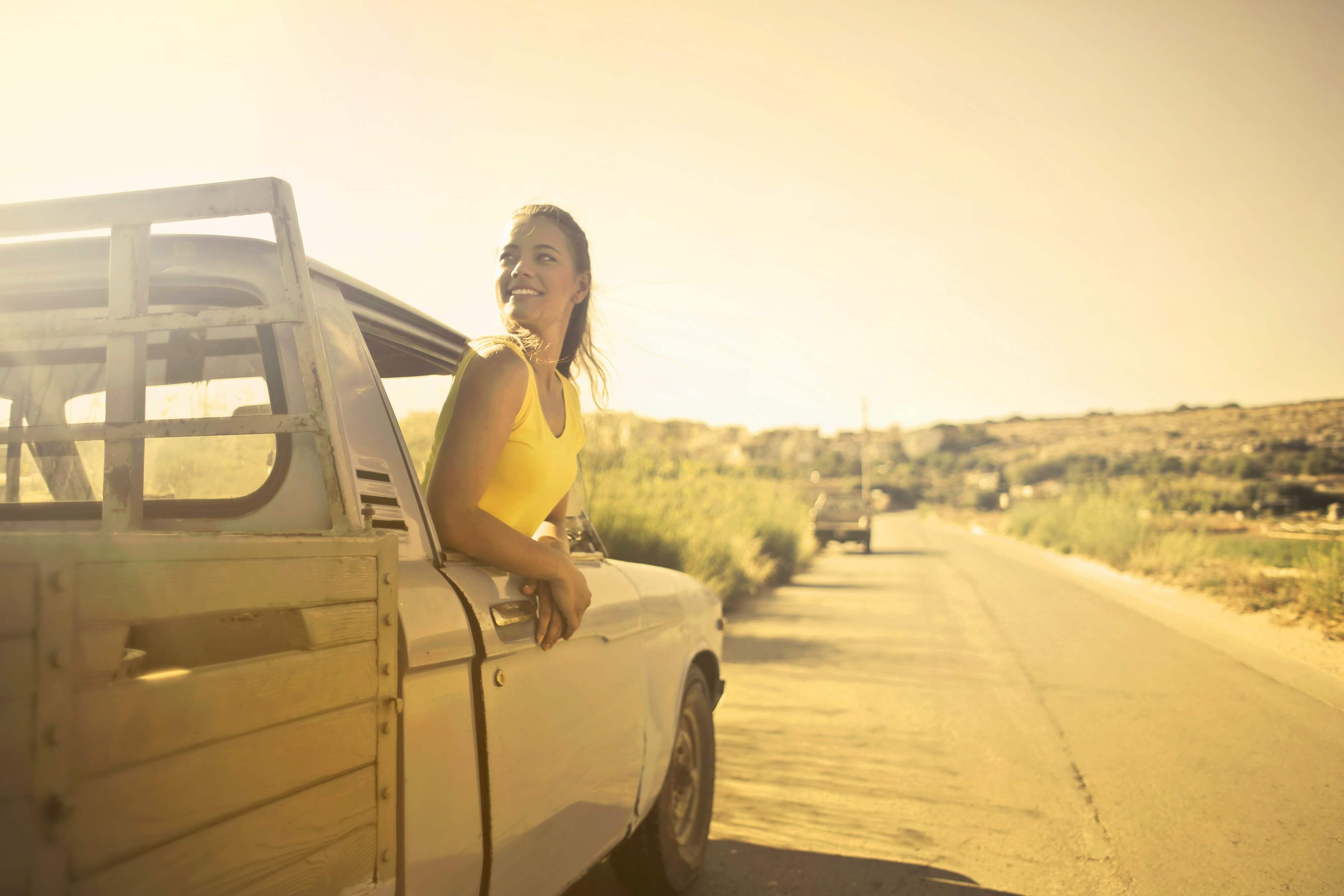 woman smiling as she hangs out the window of a car