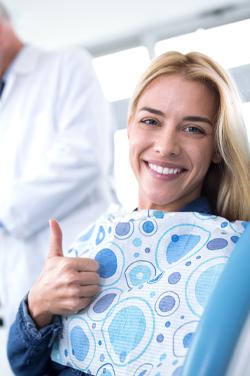women in dentist chair smiling giving a thumbs up