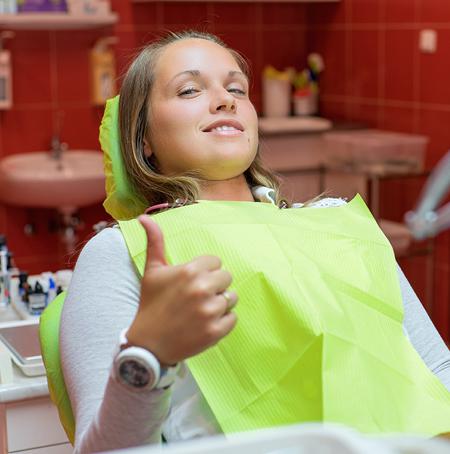 women in dentist chair happily giving a thumbs up 