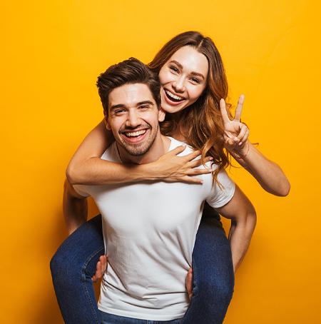 women on a mans back smiling and holding up a peace sign with her fingers 