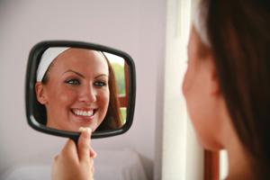 women holding hand held mirror while smiling with nice teeth