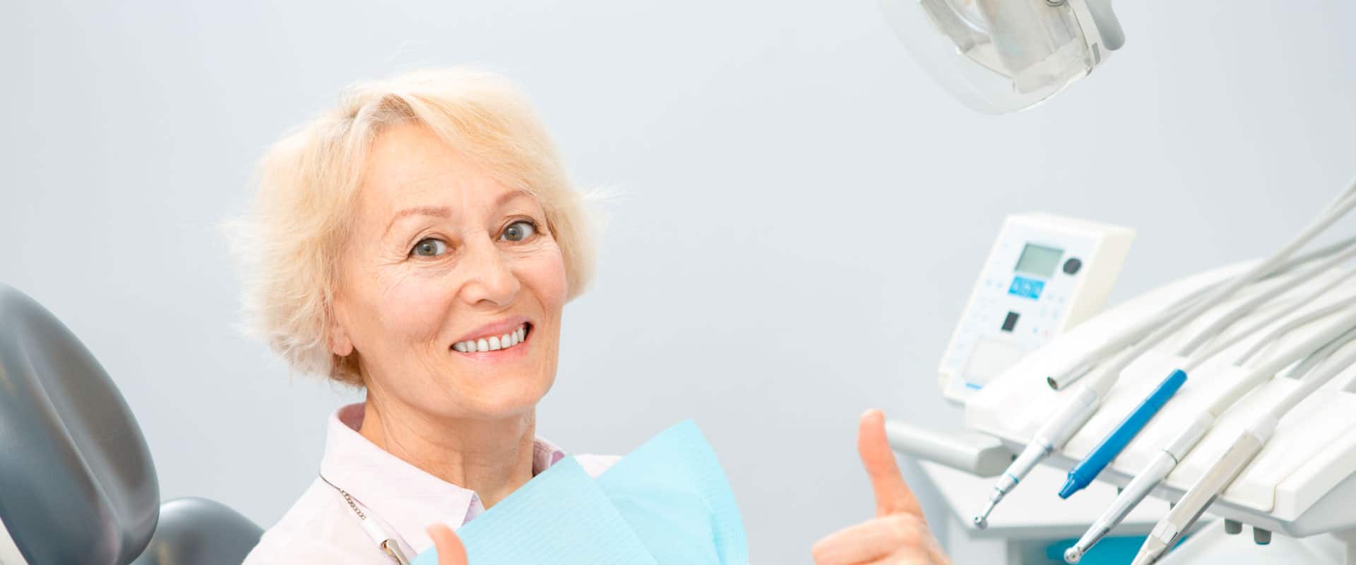 A woman sitting in a dental chair giving the thumbs up.