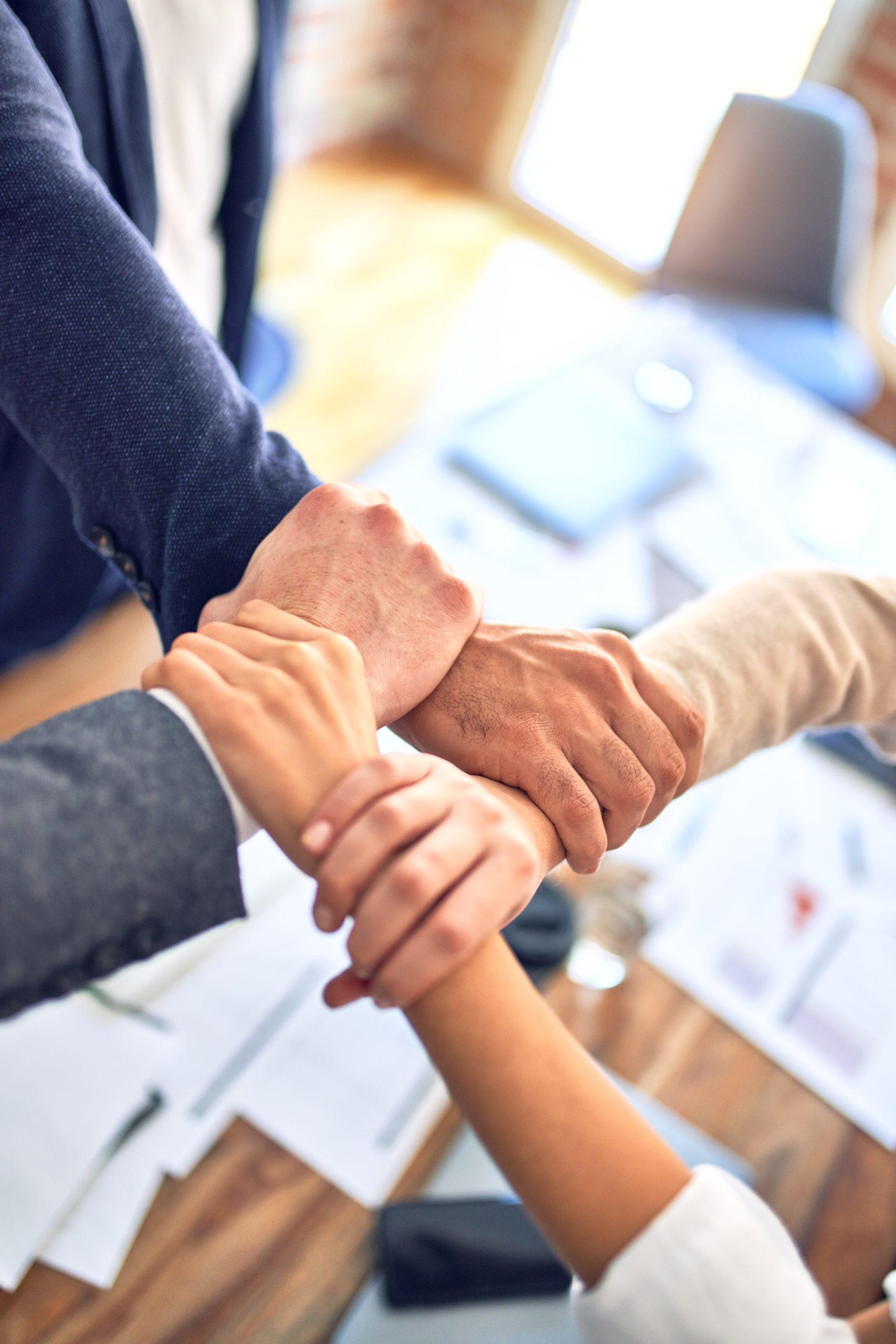 The hands of four office workers holding each other's wrists in a circle.