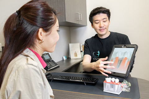 Dr. Kyubo showing a patient a display about tooth fillings.