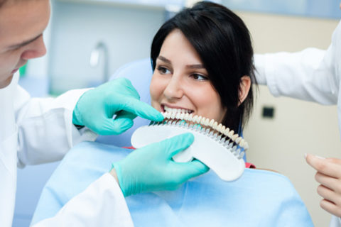 A dentist holding a dental shade guide up to a patient's teeth.