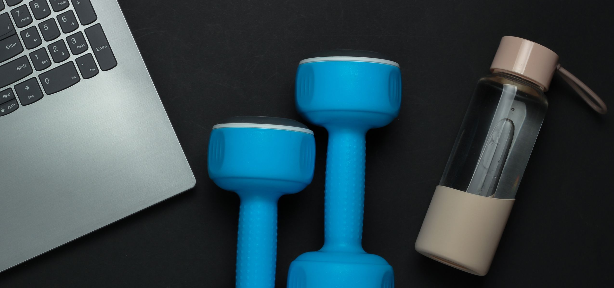 A laptop, weights and a water bottle on a tabletop.