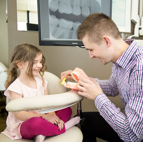 Dr. Lucas showing a child proper brushing technique with model teeth.