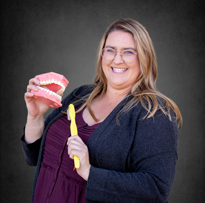 Dental Hygienist, Brianne holding a model of teeth and an oversize toothbrush.