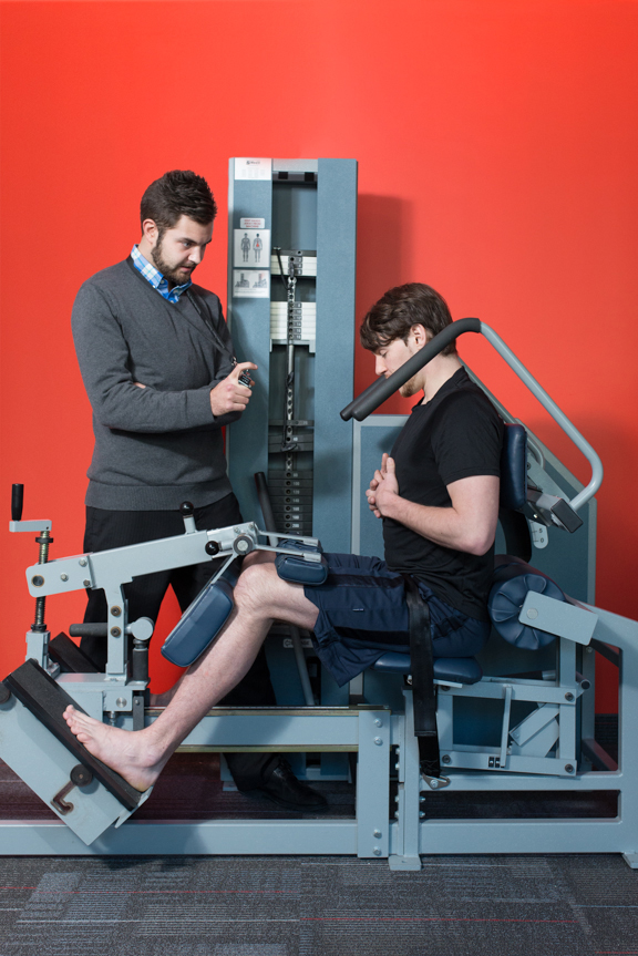 A personal trainer with a client working out on a machine.