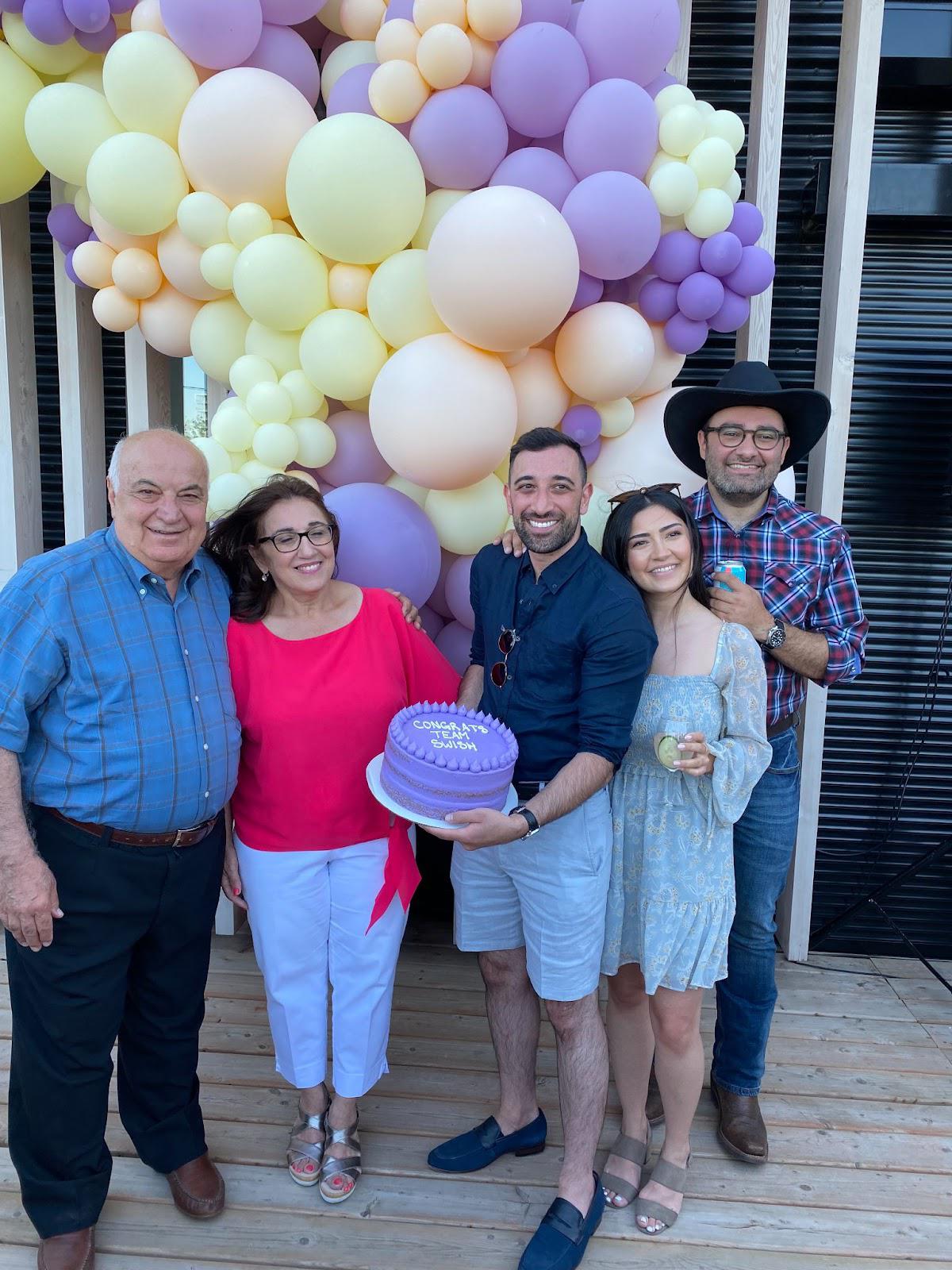 Dr. Shlah with family holding a purple cake that says 'Congrats Team Swish' in icing.