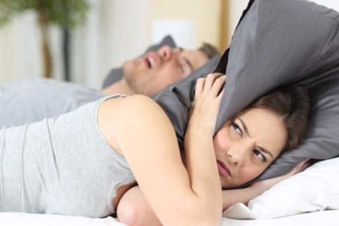 A woman covering her head with a pillow because of her partner's snoring.