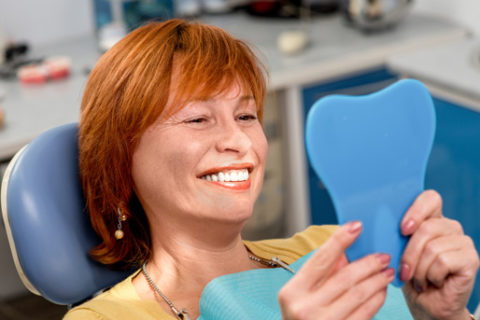 A patient with new dental implants looking in the mirror at her new smile.