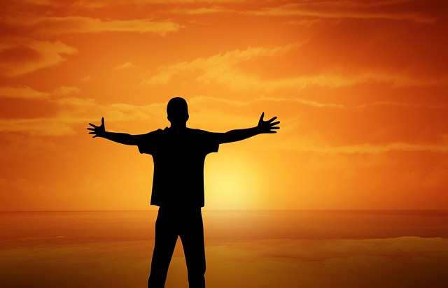 The silhouette of a person standing in a sunset with outstretched arms.