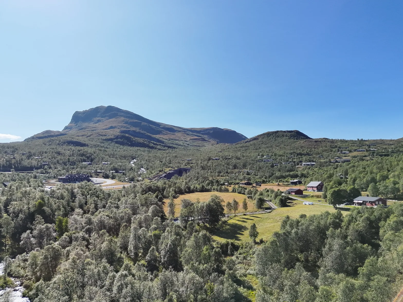 Dronebilde av Tyinkrysset med E16, fjellstua, hytter og skog, og Skørsnøse i bakgrunnen