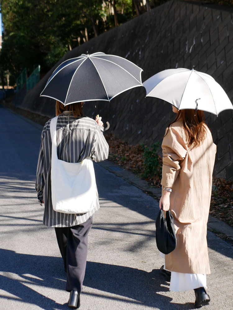 黒と灰色のビコーズプレーンパイピング傘をハンドバッグとともに持ち、オーバーコートを着て歩くファッショナブルな女性