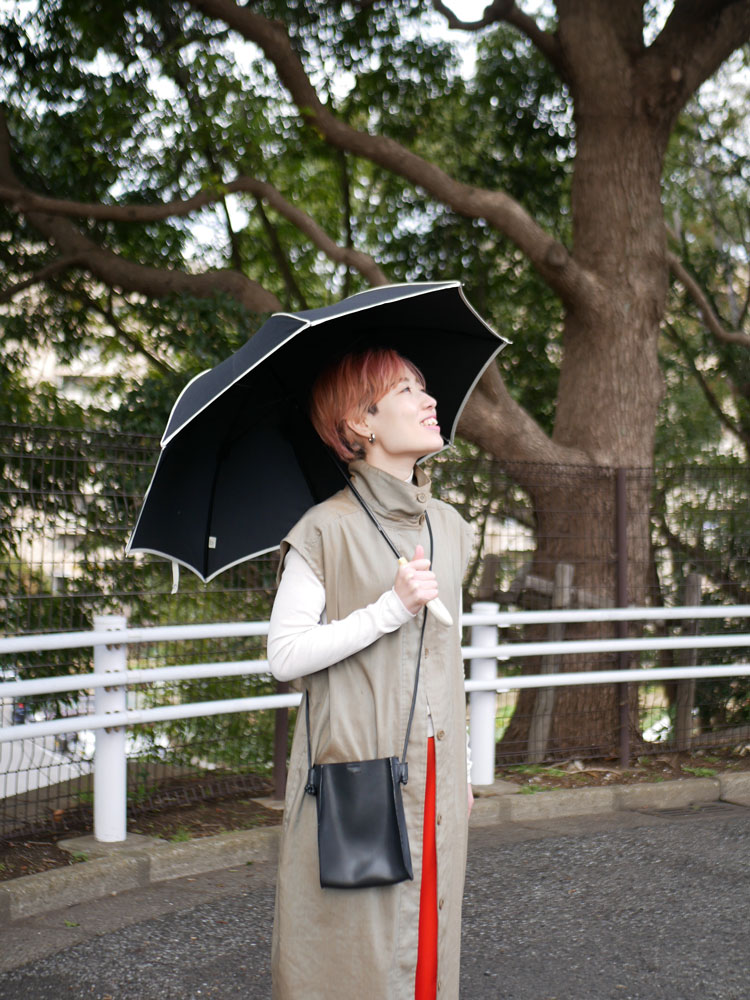 ビコーズのプレーンパイピング傘を携え、オーバーコートとハンドバッグを持って歩くファッションモデル