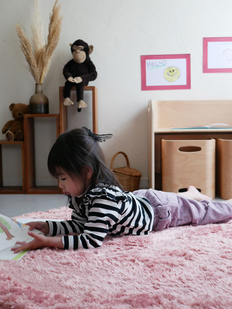 ピンク色の直径130cmホップル円形ラグが床に敷かれ、その上に子供用のおもちゃや衣類が配置された様子