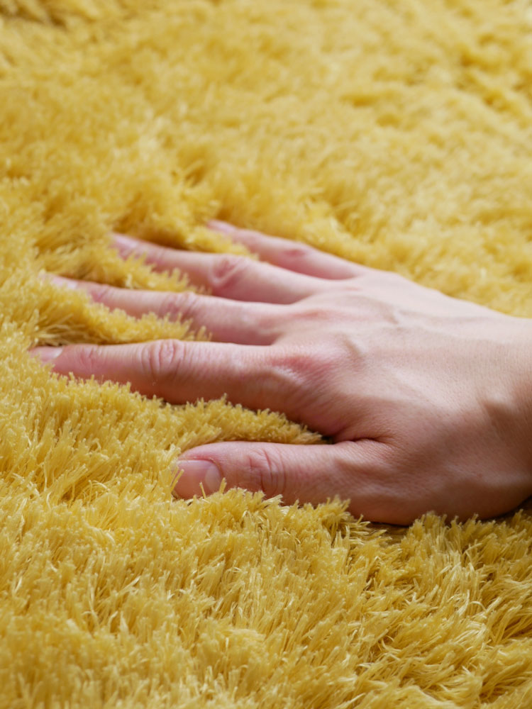 リビングルームの木製床に敷かれた黄色い130cmの円形ラグ